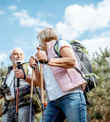 elderly couple hiking with sticks and rucksacks
			                        