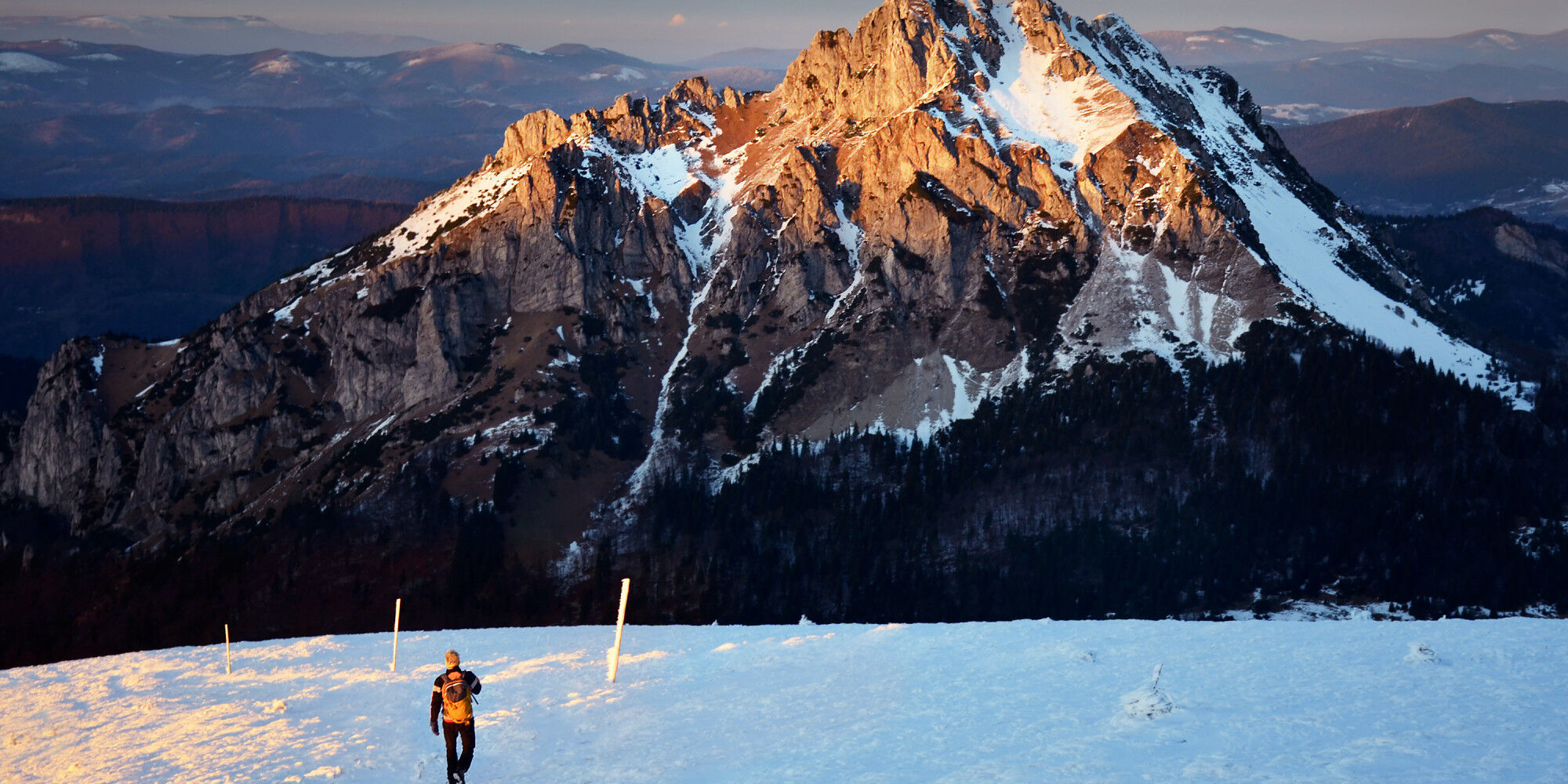 snow-covered mountain with the setting sun beating down and a person taking a walk
				        