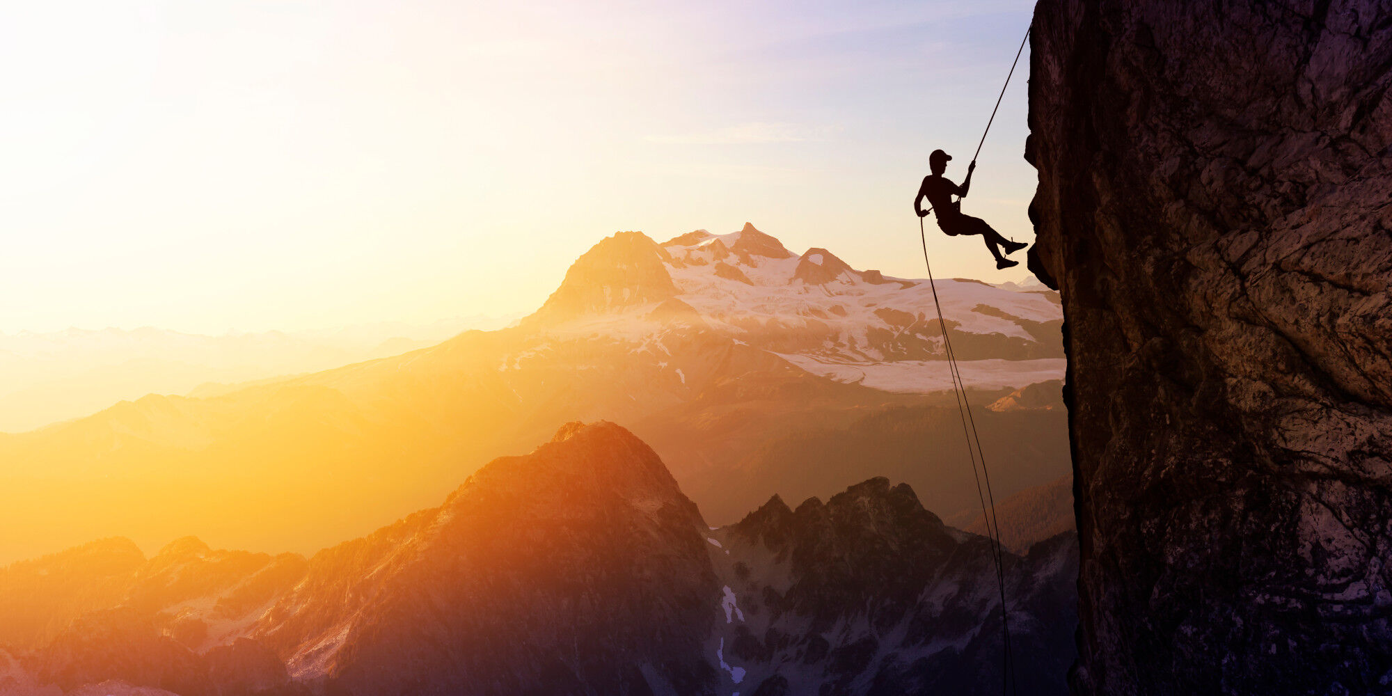 personne qui descend une falaise en rappel avec un coucher de soleil