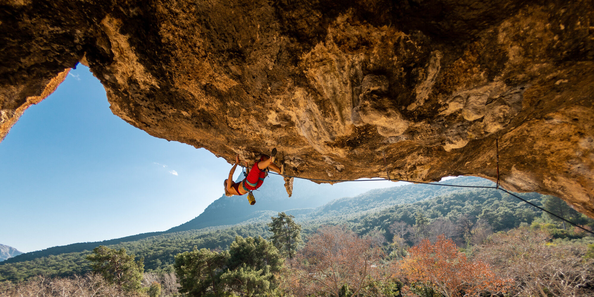 homme qui escalade une falaise à l'horizontale avec un baudrier
				        