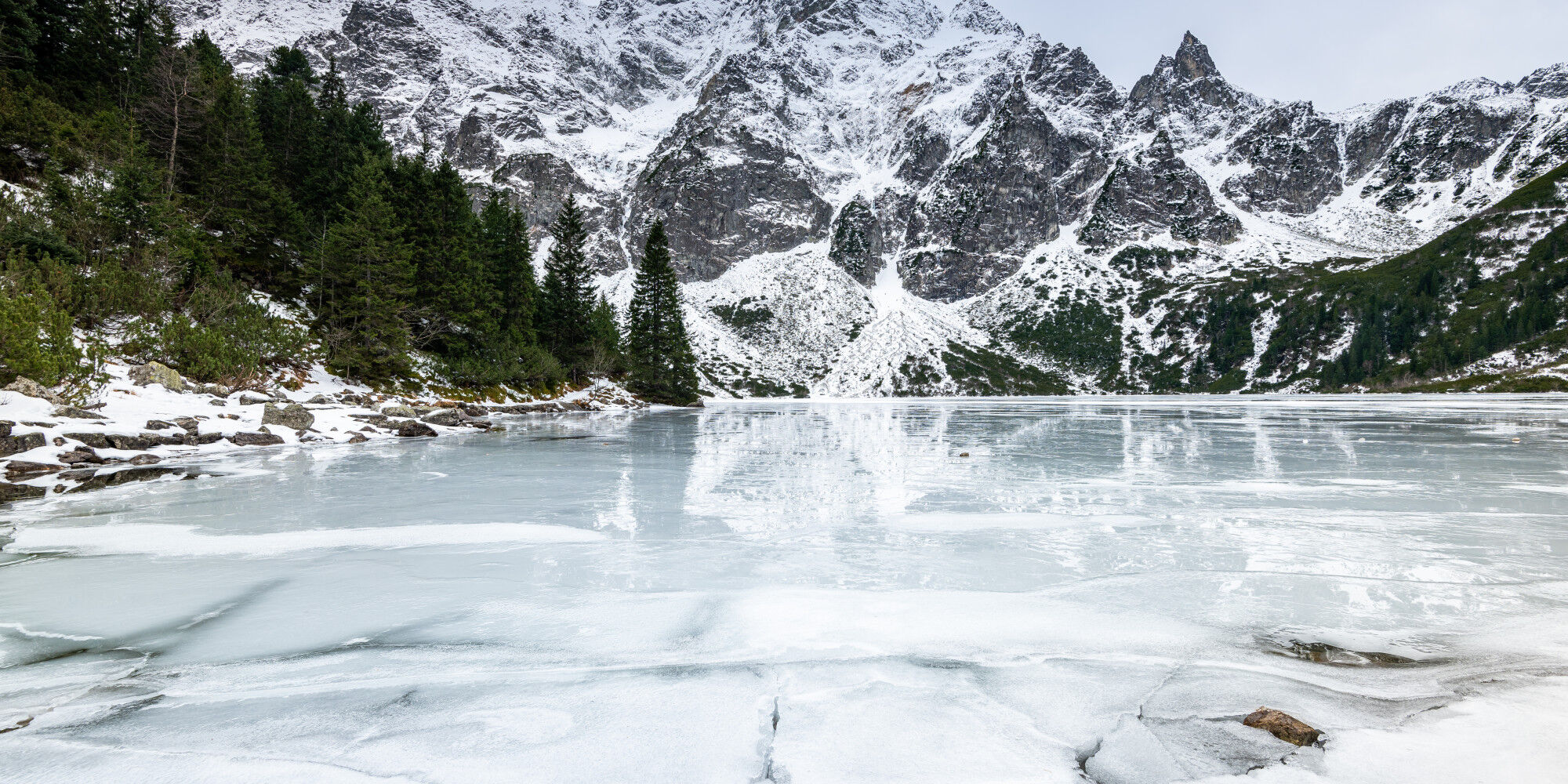 lac gelé dans la montagne avec de la roche et des forêts de pins
				        