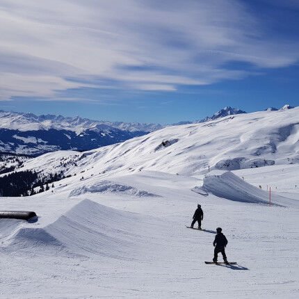 pistes en montagne avec deux snowboarders et la forêt
			                    
