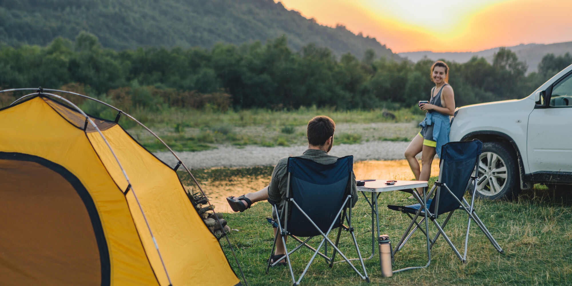 couple camping with a tent, table and chairs
				        