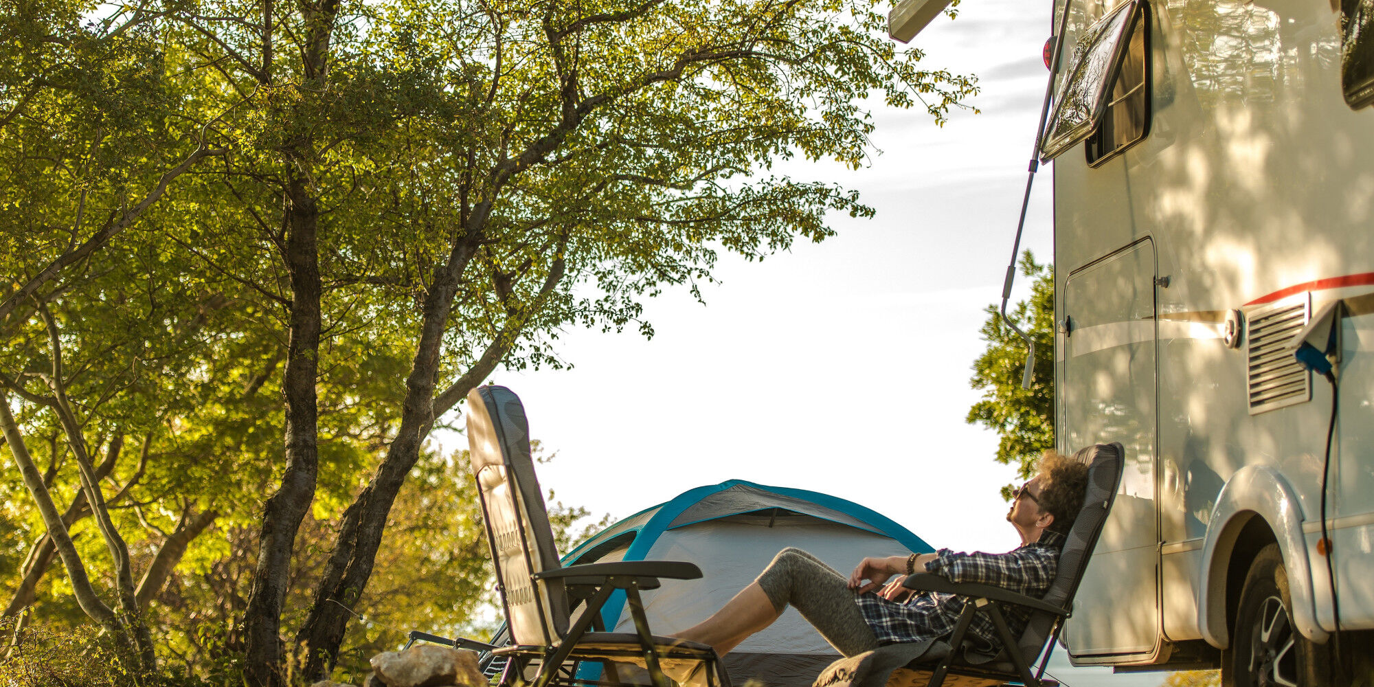 Camper, der sich neben seinem Zelt und Wohnwagen ausruht
				        