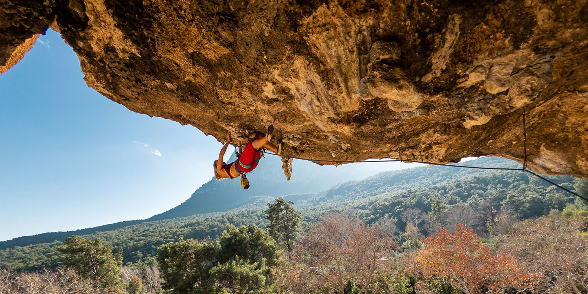 woman climbing a cliff with a chalk bag
				        