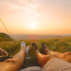 LENS FLARE: Man and woman on summer hiking trip relax and watch the sunrise.
			                