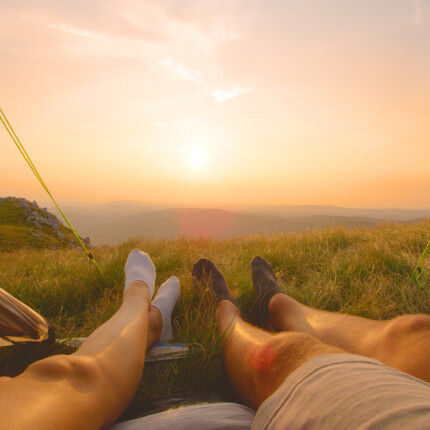 LENS FLARE: Man and woman on summer hiking trip relax and watch the sunrise.
			                    