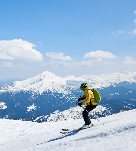 yellow skier racing down the ski slopes and you can see the mountains
			                        