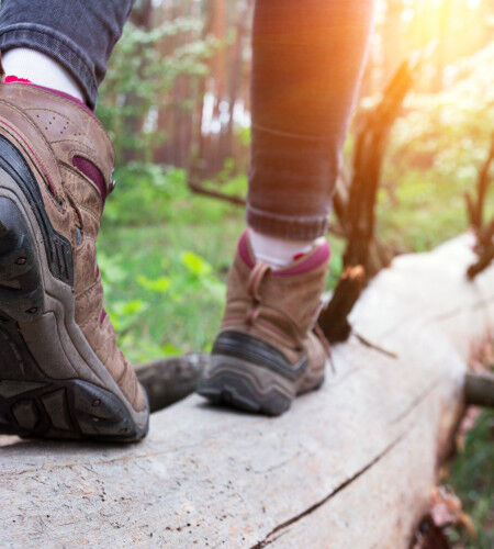 woman in hiking boots walking on a tree trunk
			                        